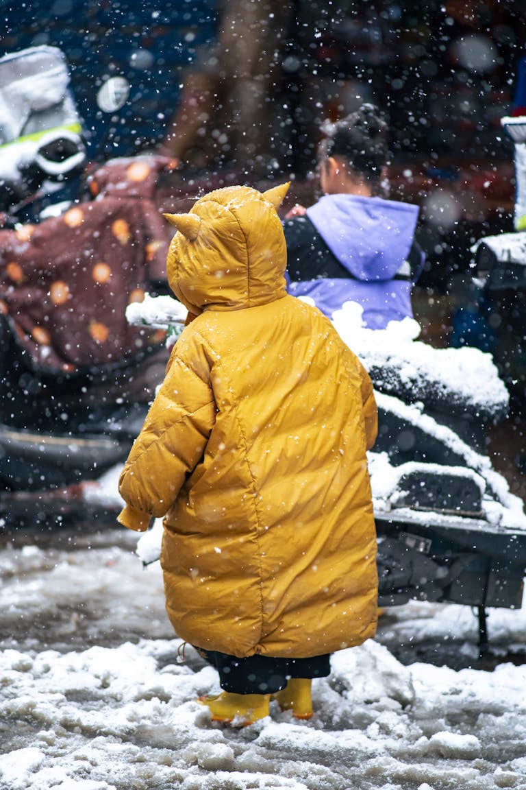 A child in a yellow jacket stands in falling snow, capturing the essence of winter.
