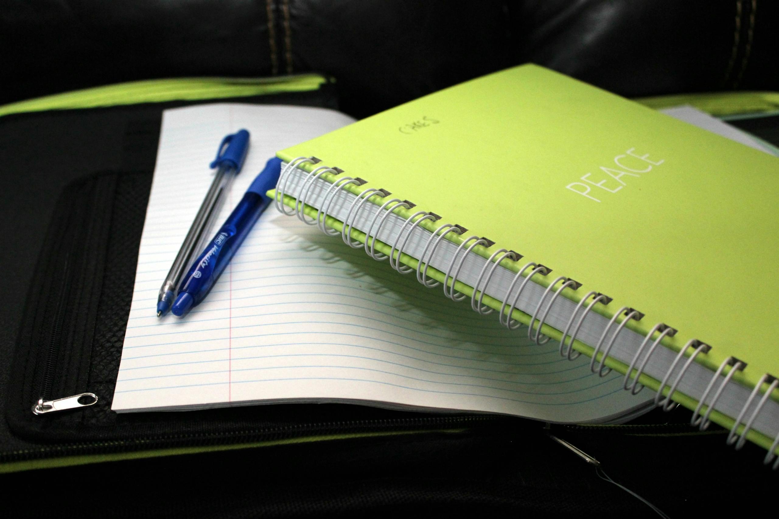 Green spiral notebook labeled 'PEACE' with pens on lined paper.